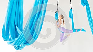 Beautiful young woman smiling at practicing aero fly yoga in white studio on blue hammocks. Concept stretching