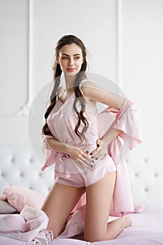 Beautiful young woman smiling sensually on the bed playing with her pink pajama set