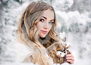 Beautiful young woman in snow forest with a cotton branch. Winter beauty portrait