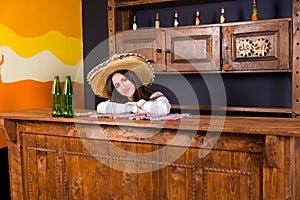 Beautiful young woman in a sombrero leaned on bar counter in Mex