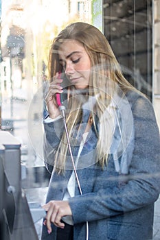 Beautiful young woman speaking on a public payphone