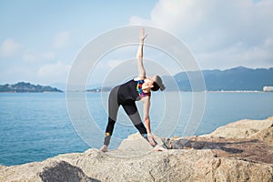 Beautiful young woman in sports jumpsuit doing yoga exercise outdoors with sea views