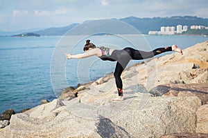 Beautiful young woman in sports jumpsuit doing yoga exercise outdoors with sea views