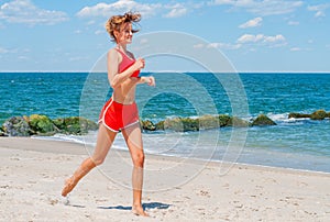 Beautiful young woman in sportswear jogging on beach.