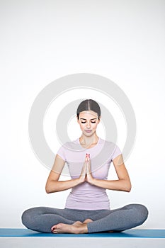 Beautiful young woman in sportswear practicing yoga while sitting in lotus position on white background