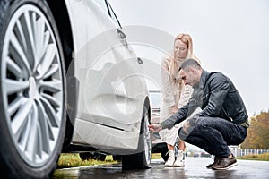 Young man helping charming woman to fix car wheel.