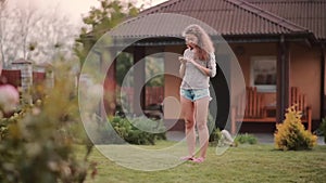 Beautiful young woman standing on the backyard and uses the smartphone. Female browse the Internet on mobile phone.