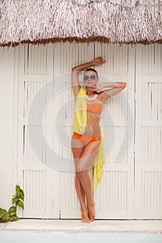 Beautiful young woman standing in an orange bikini while sunbathing on a white backgroundl