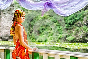 A beautiful young woman is standing on a pier looking at the lake with lotus