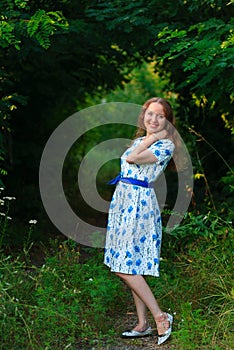 Beautiful young woman standing with a smile. Portrait of a beautiful girl in white dress among trees in the forest. Girl.