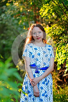 Beautiful young woman standing with a smile. Portrait of a beautiful girl in white dress among trees in the forest. Girl.