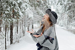 Beautiful young woman standing among snowy trees in winter forest and enjoying snow.