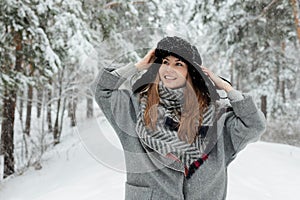 Beautiful young woman standing among snowy trees in winter forest and enjoying snow.