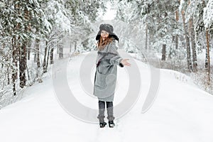 Beautiful young woman standing among snowy trees in winter forest and enjoying snow.