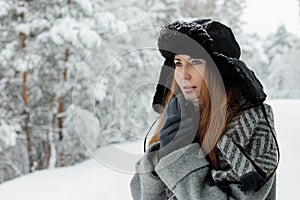 Beautiful young woman standing among snowy trees in winter forest and enjoying snow.