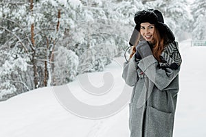 Beautiful young woman standing among snowy trees in winter forest and enjoying snow.