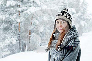 Beautiful young woman standing among snowy trees in winter forest and enjoying snow