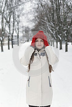 Beautiful young woman standing and straightens his hat among the snowy trees in the winter forest. Vertical frame