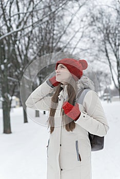 Beautiful young woman standing and straightens his hat among the snowy trees in the winter forest. Vertical frame