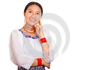 Beautiful young woman standing wearing traditional andean blouse and red necklace, resting head on hand while smiling