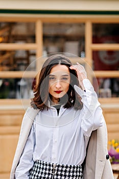 Beautiful young woman stands on the street and straightens her hair, brunette looks at the camera