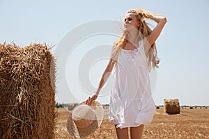 Beautiful young woman with straw hat near rolled hay bale on sunny day