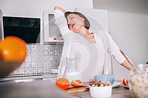Beautiful young woman stretching after awakening and yawning at modern kitchen. New day beginning concept image
