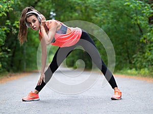 Beautiful young woman stretching muscles before jogging in forest.