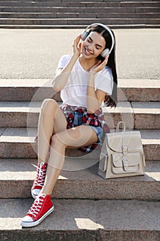 Beautiful young woman with stylish beige backpack and headphones on stairs outdoors