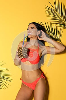 Beautiful young woman in stylish bikini with cocktail and tropical leaves