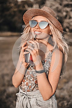 Beautiful young woman in stylish hat with cold cocktail has a fun outdoors.