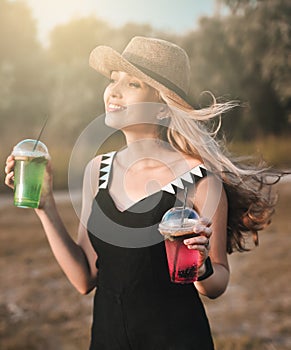 Beautiful young woman in stylish hat with cold cocktail has a fun outdoors.