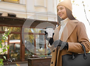 Beautiful young woman with stylish leather gloves and cup of coffee on city street