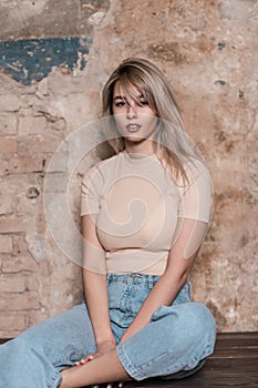 Beautiful young woman in a stylish T-shirt in blue fashionable jeans with a trendy hairstyle posing near a brick wall in the