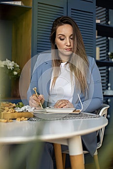 Beautiful young woman in suit writing her business plans while drinking coffee on break time