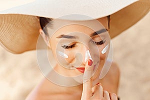 Beautiful Young woman with sun cream on face. Girl holding sunscreen bottle on the beach