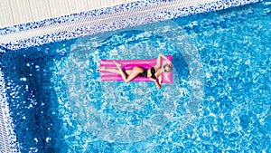 Beautiful young woman sunbathing on inflatable pink mattress at pool