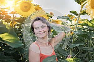 Beautiful young woman with sunflowers enjoying nature and laughing on summer sunflower field. Woman holding sunflowers