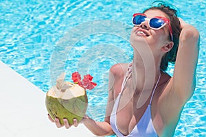 Beautiful young woman in sunglasses with coconut cocktail in hand in luxury pool