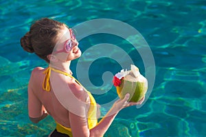 Beautiful young woman in sunglasses with coconut cocktail in hand in luxury pool