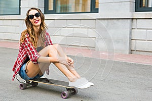 Beautiful young woman in sunglasses seat on skate, street fashion lifestyle.