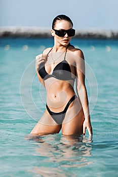 Beautiful young woman with sunglasses in sexy bikini standing at sea beach