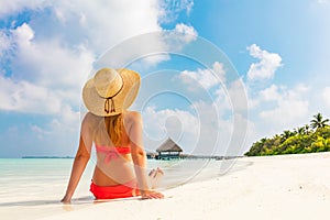 Beautiful young woman in sunhat sitting relaxed on tropical beach in Maldives
