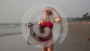 A beautiful young woman surfer walks in the evening on a sandy sea beach