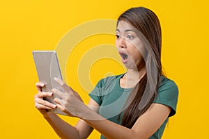 Beautiful young woman surprised facial expression after seeing shocking, amaze deal in mobile phone isolated on yellow background.