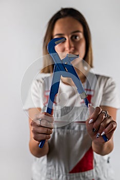 beautiful young woman in suspenders holds a blue wrench in her hands.