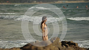 Beautiful young woman in swimsuit and sunglasses slowly walks into the water.