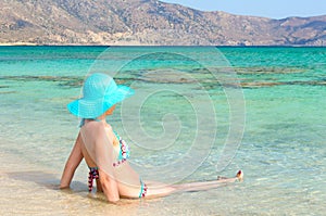 Beautiful young woman in swimsuit with sunhat, relaxing on the sunny beach