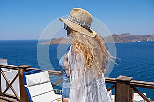 Beautiful young woman in swimsuit white dress and straw hat on white terrace balcony of house or hotel with Sea View