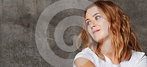 Beautiful young woman in T-shirt looking away at the camera isolated against concrete wall background.